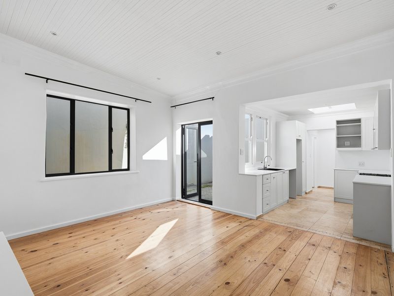 Bright open-plan living area featuring polished timber floors, beadboard ceilings, and a modern kitchen with clean cabinetry and a skylight.