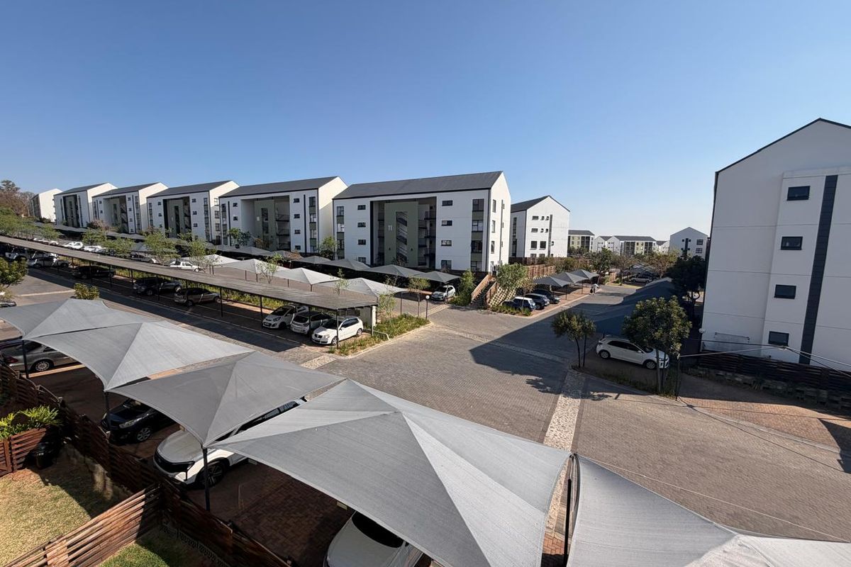 Aerial view of a modern apartment complex featuring paved driveways and covered shade cloth parking bays for residents.