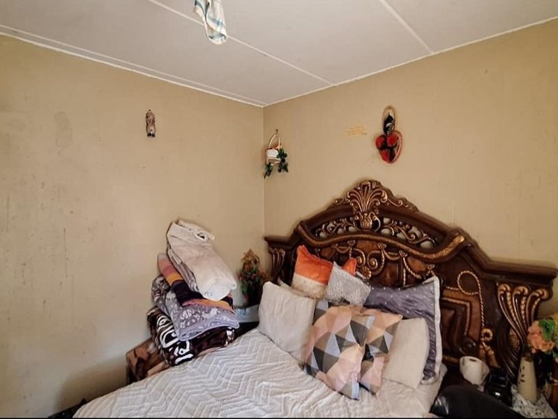 A bedroom featuring plain wall finishes and a standard electrical outlet, currently showing signs of wear on the wall surfaces.
