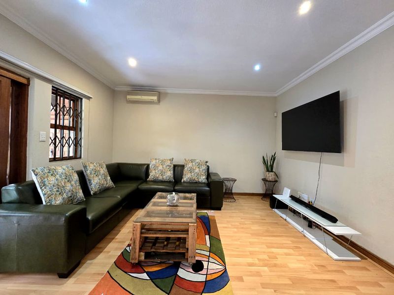 A well-maintained living room featuring laminate flooring, recessed downlighting, coving, and a wall-mounted split-system air conditioning unit.