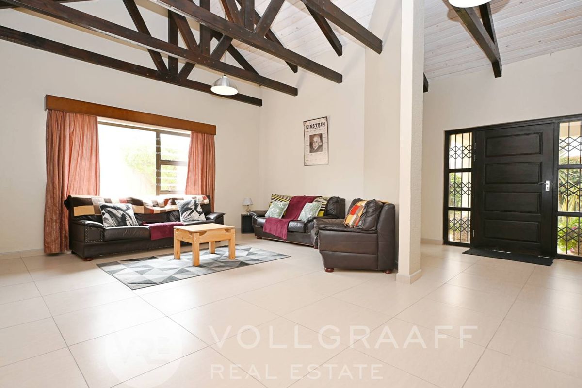 Spacious living area featuring high vaulted ceilings with exposed timber trusses, tiled flooring, and a secure entrance door with security gate.