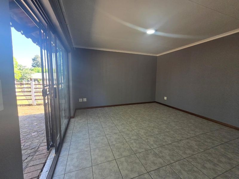 A bright, empty living room featuring neutral grey walls, ceramic floor tiles, and a large sliding glass door providing access to the outdoor area.