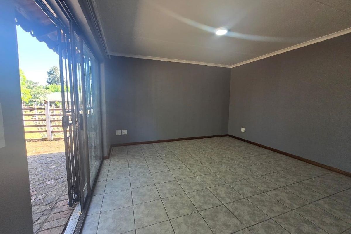 A bright, empty living room featuring neutral grey walls, ceramic floor tiles, and a large sliding glass door providing access to the outdoor area.