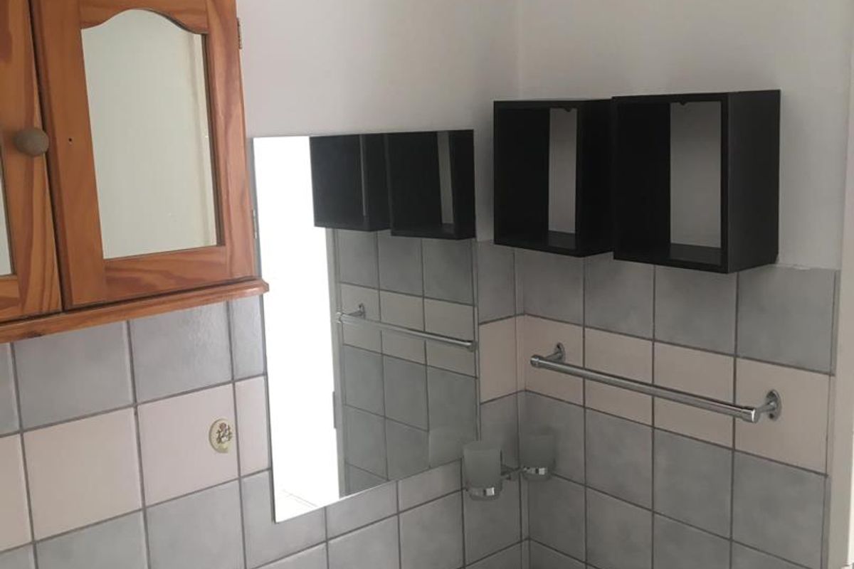 A functional bathroom featuring a wall-mounted basin, tiled walls, and basic fixtures, showing signs of wear and dated finishes.