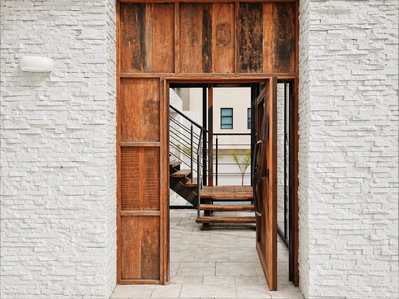 A modern entrance featuring a rustic timber door framed by white stacked stone cladding, leading to an outdoor staircase area.
