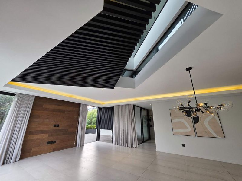 Spacious modern living area featuring a striking slatted timber ceiling, integrated skylight, recessed ambient lighting, and large format floor tiles with seamless outdoor access.