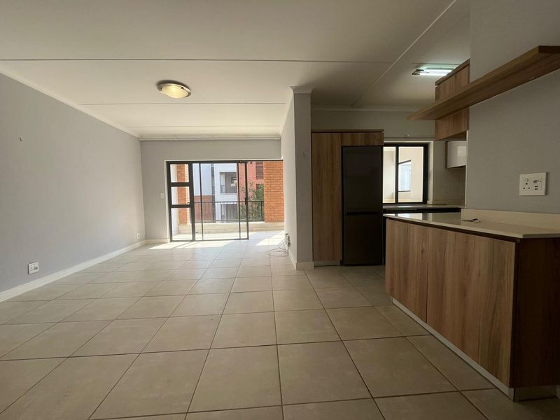 An open-plan living and kitchen area featuring neutral tiled flooring, modern wood-finish cabinetry, and direct access to a balcony through sliding glass doors.