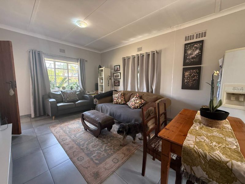 A comfortable living room featuring tiled flooring, coved ceilings, and natural light through a window with security bars.