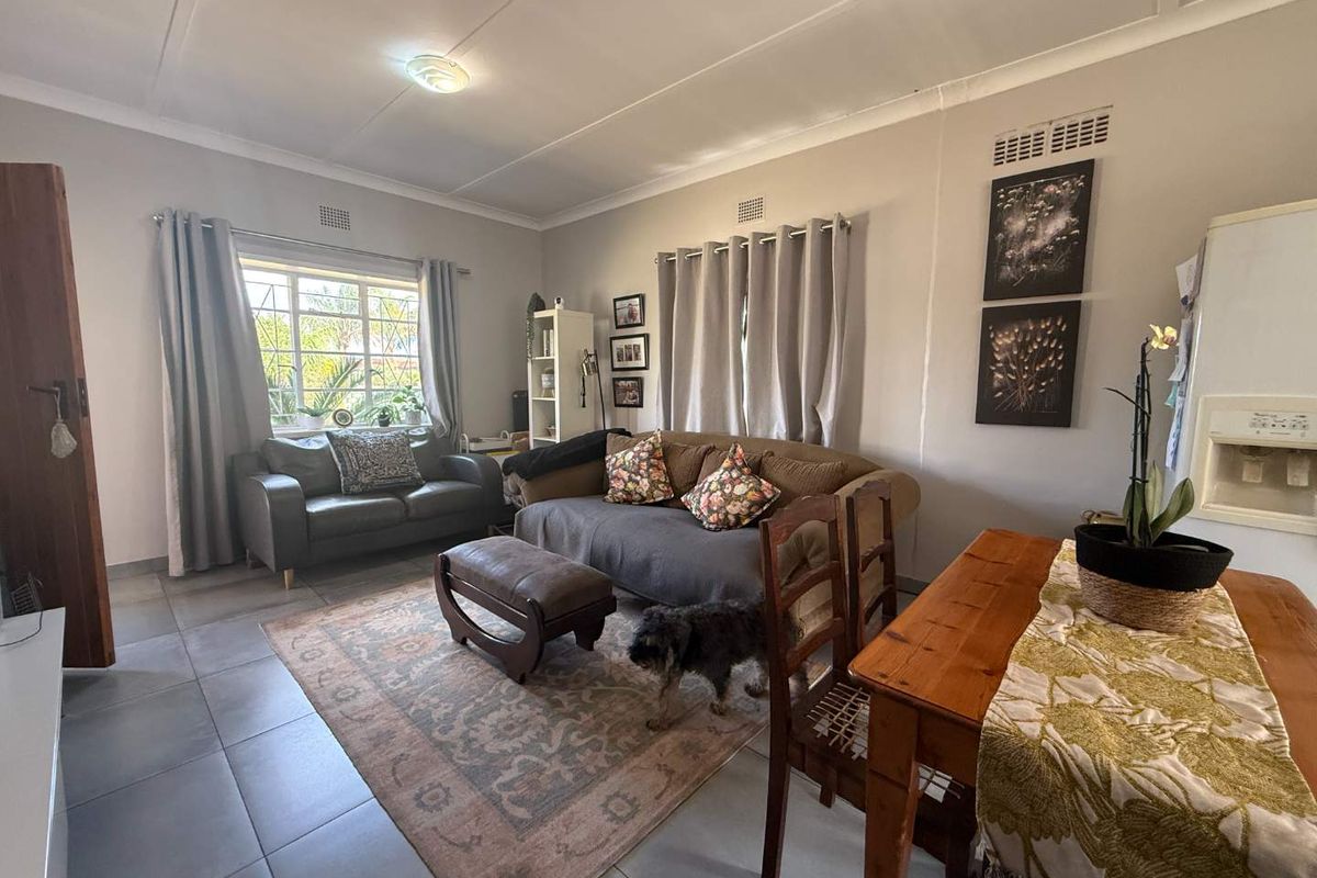 A comfortable living room featuring tiled flooring, coved ceilings, and natural light through a window with security bars.