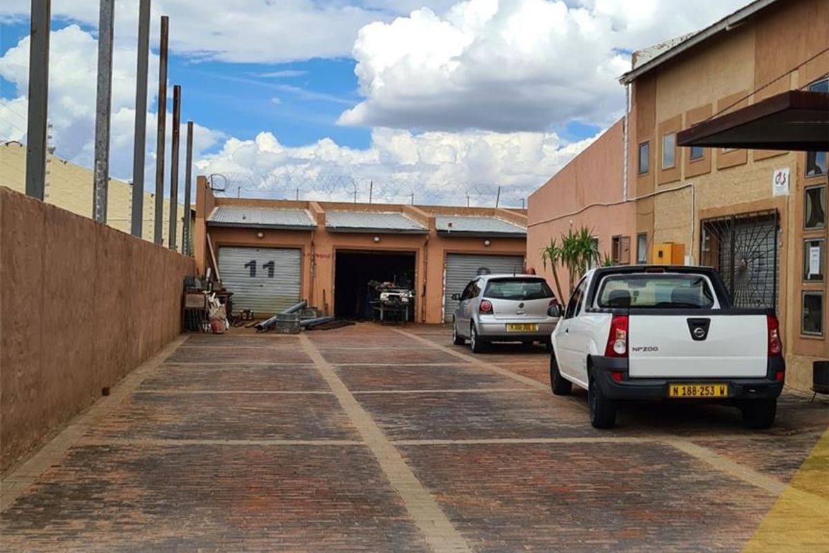 Exterior view of a mixed-use property featuring a paved driveway, multiple garage access points, and perimeter security fencing.