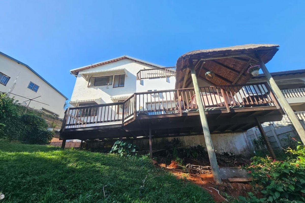 Rear view of the property featuring a raised timber deck with a thatched gazebo, overlooking a sloped garden area.