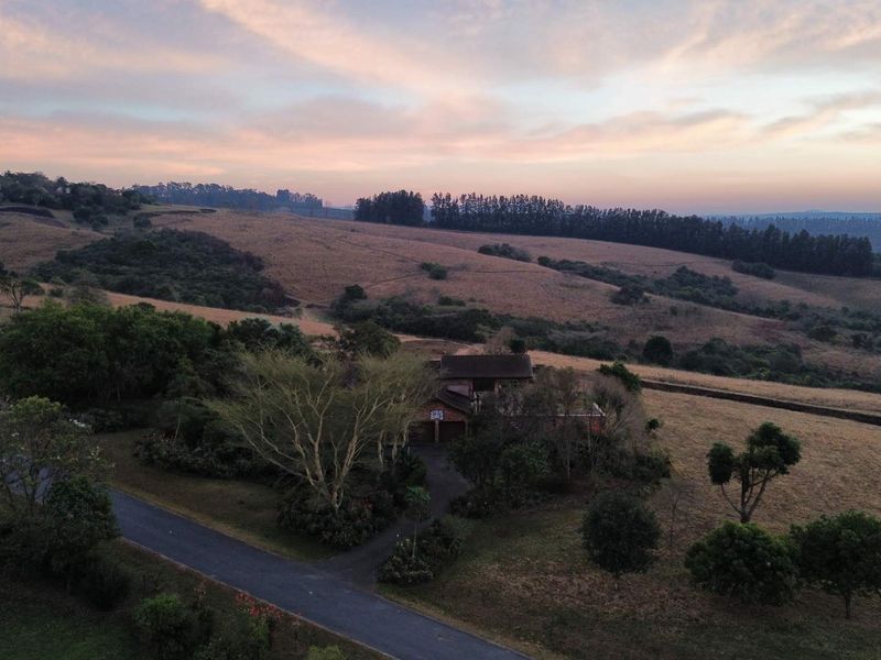 Aerial view of a residential property set within a vast, rolling landscape at sunset, featuring a private driveway and established garden surroundings.