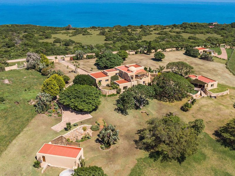 Aerial view of a coastal small holding featuring a main residence, outbuildings, swimming pool, and expansive landscaped grounds overlooking the ocean.