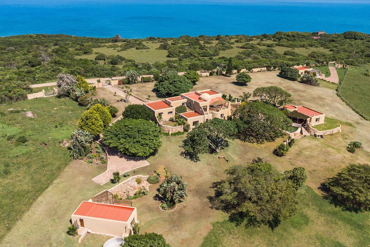 Aerial view of a coastal small holding featuring a main residence, outbuildings, swimming pool, and expansive landscaped grounds overlooking the ocean.