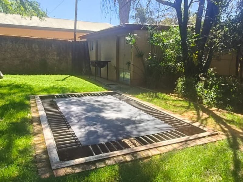 A spacious backyard garden featuring a sunken in-ground trampoline, established lawn, perimeter boundary wall, and a detached outbuilding.