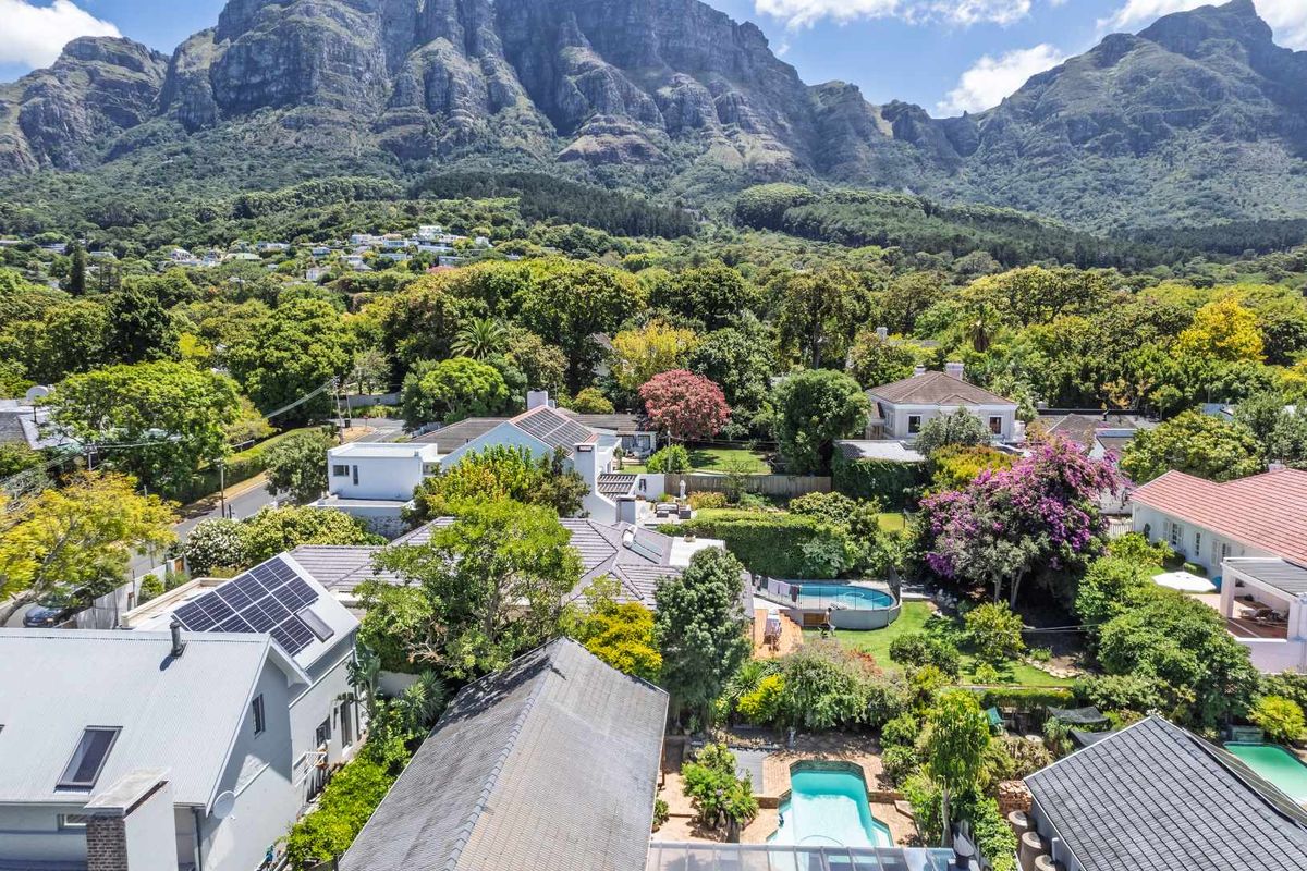 Aerial view of a residential property featuring multiple swimming pools, solar panels, and lush garden surroundings set against a mountain backdrop.