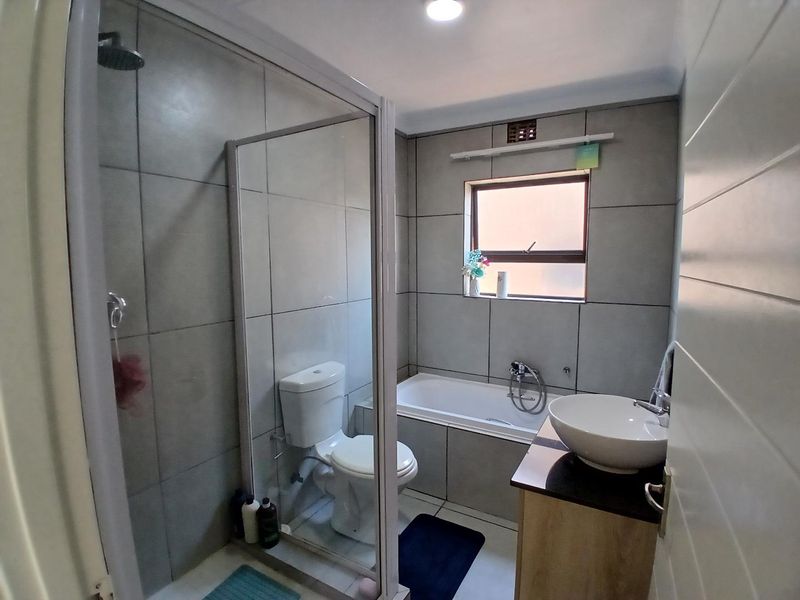 A modern bathroom featuring a glass-enclosed shower, a built-in bathtub, a vessel sink vanity, and neutral grey wall tiling.