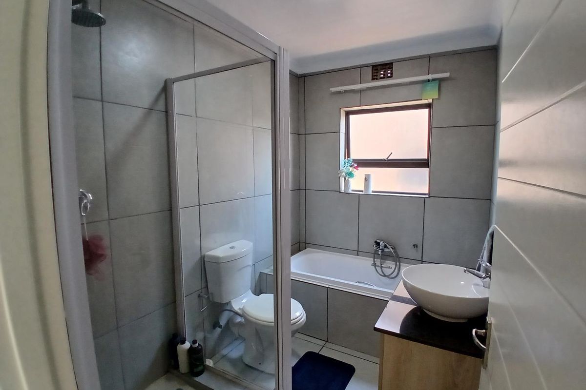 A modern bathroom featuring a glass-enclosed shower, a built-in bathtub, a vessel sink vanity, and neutral grey wall tiling.
