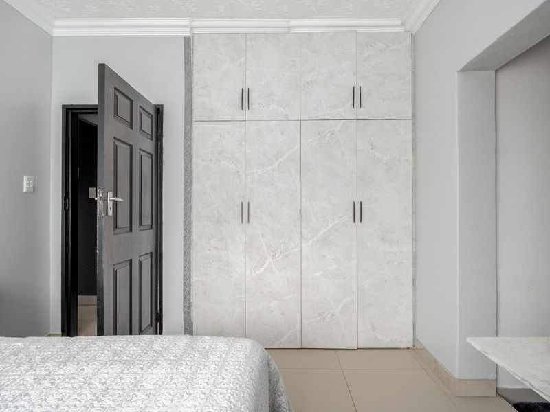A bedroom featuring modern marble-effect built-in cupboards, tiled flooring, and decorative ceiling cornicing.