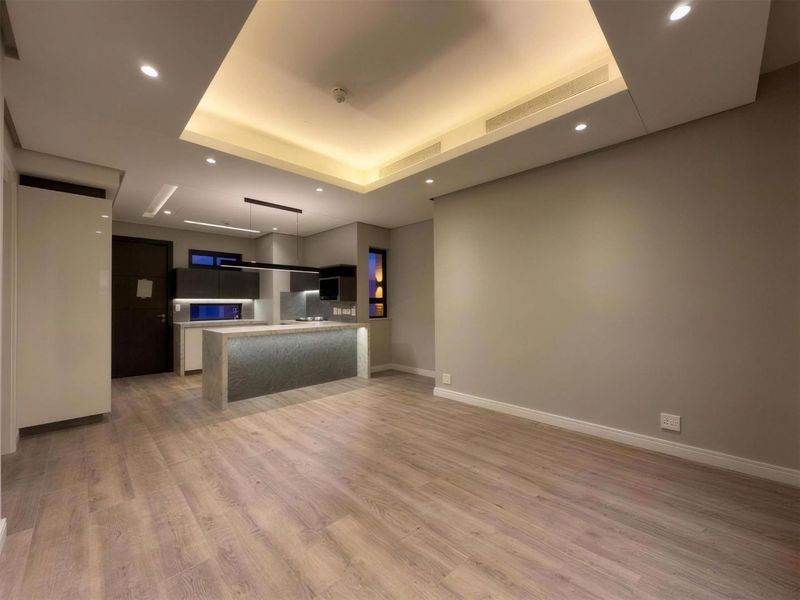 Modern open-plan living area featuring a sleek kitchen island, recessed ceiling lighting with cove accents, and high-quality laminate flooring throughout.