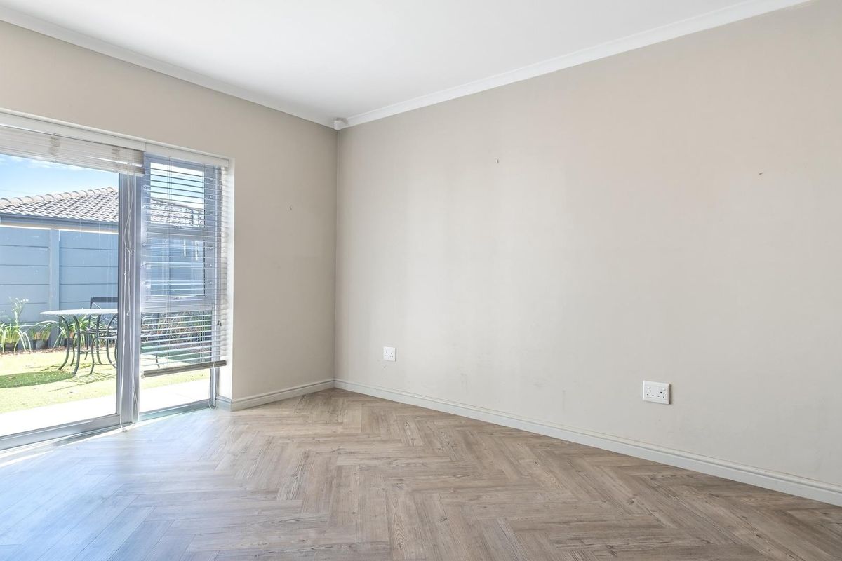 A bright, empty living room featuring herringbone-patterned wood-look flooring and a sliding glass door providing direct access to the rear garden.