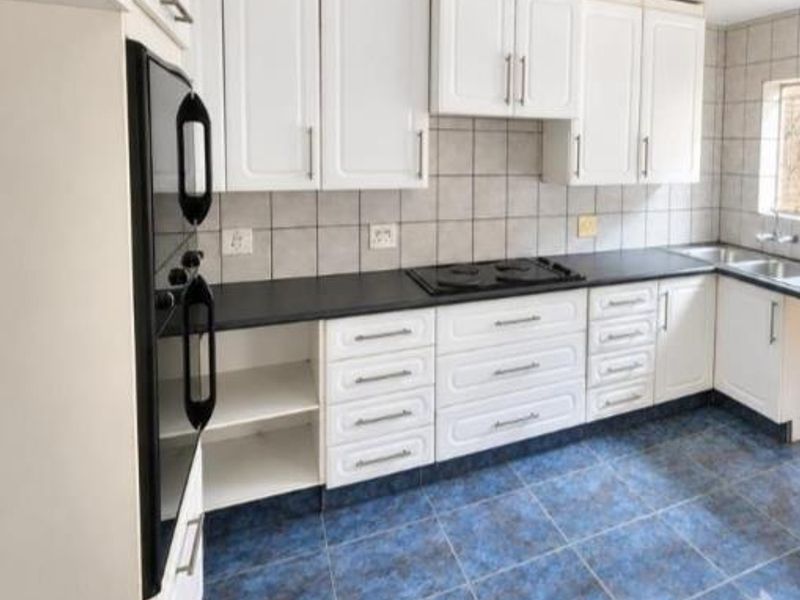 A functional kitchen featuring white cabinetry, black countertops, built-in oven, electric hob, and tiled finishes throughout.