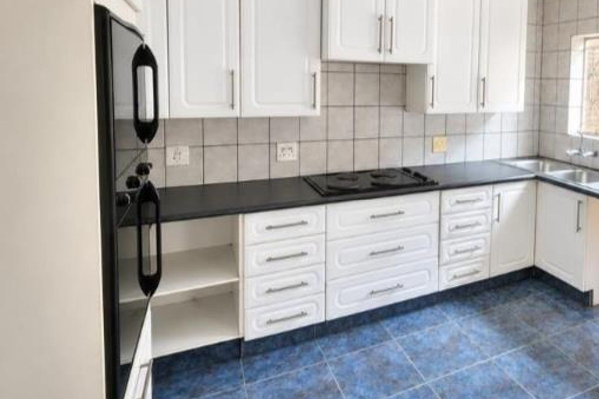 A functional kitchen featuring white cabinetry, black countertops, built-in oven, electric hob, and tiled finishes throughout.