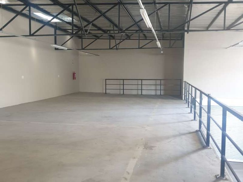 Spacious industrial mezzanine level featuring exposed steel roof trusses, concrete flooring, and secure metal safety railings, suitable for storage or workspace.