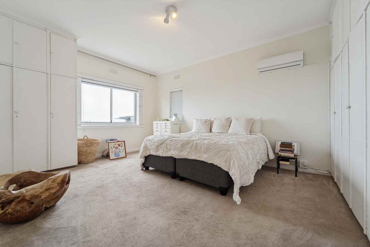 A spacious bedroom featuring wall-to-wall built-in wardrobes, neutral carpeting, and a wall-mounted air conditioning unit.