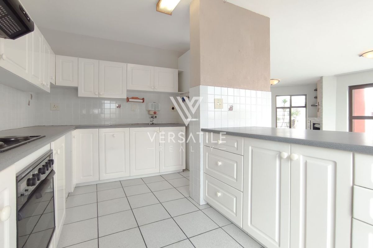 A functional kitchen featuring white cabinetry, tiled splashbacks, a built-in oven, and a breakfast bar counter, opening into the adjacent living area.