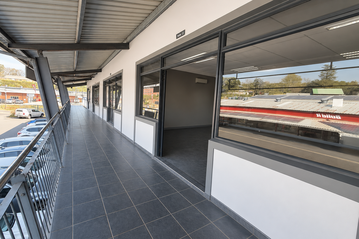 An exterior walkway balcony featuring tiled flooring, metal balustrades, and aluminum-framed glass access points to the commercial suite.