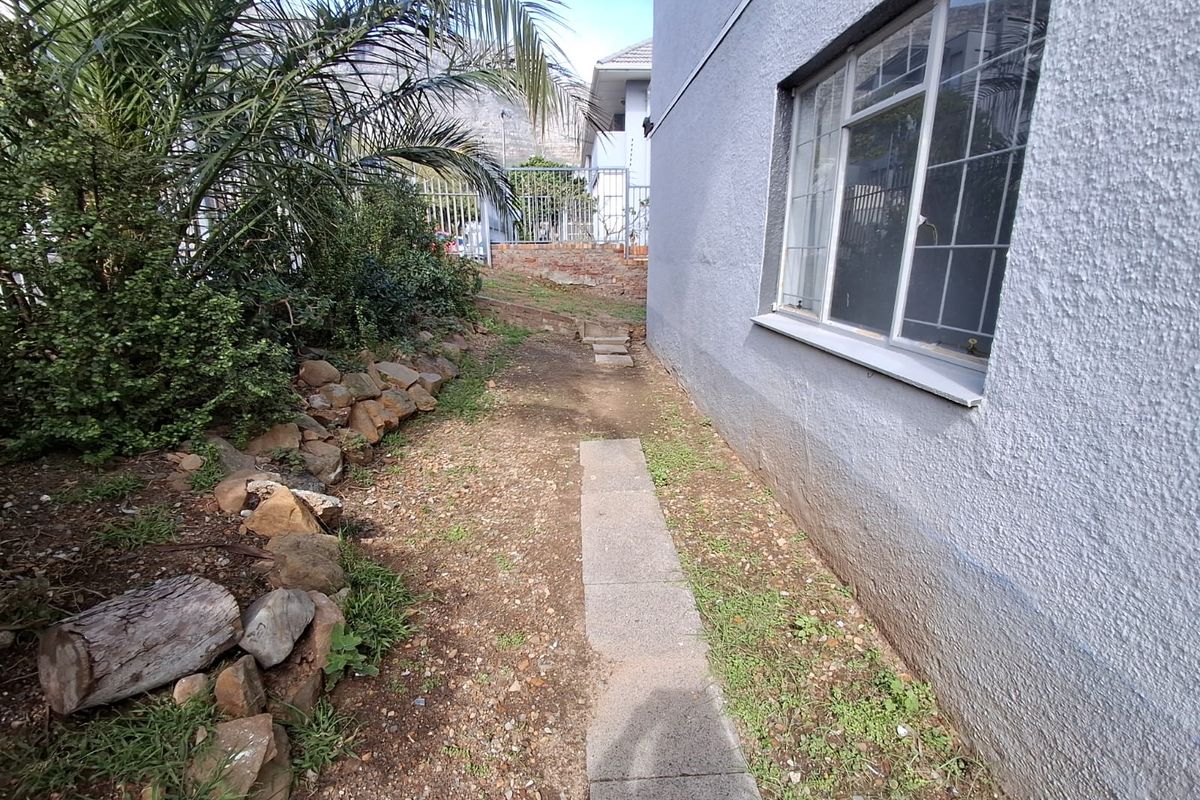 A side exterior view of the apartment building featuring a concrete pathway, rock retaining wall, and metal security fencing along the perimeter.