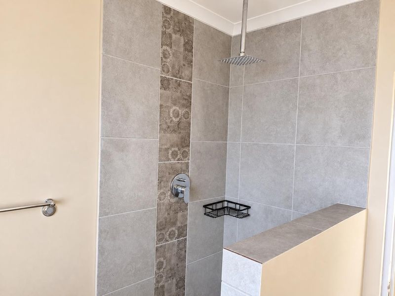 A modern walk-in shower featuring large format grey wall tiles, a decorative vertical tile inlay, and a contemporary square rain shower head.