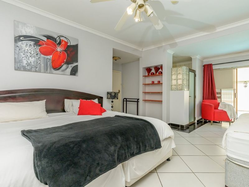 Spacious bedroom featuring tiled flooring, a ceiling fan, built-in shelving, and a glass block partition leading to an adjoining area with patio access.