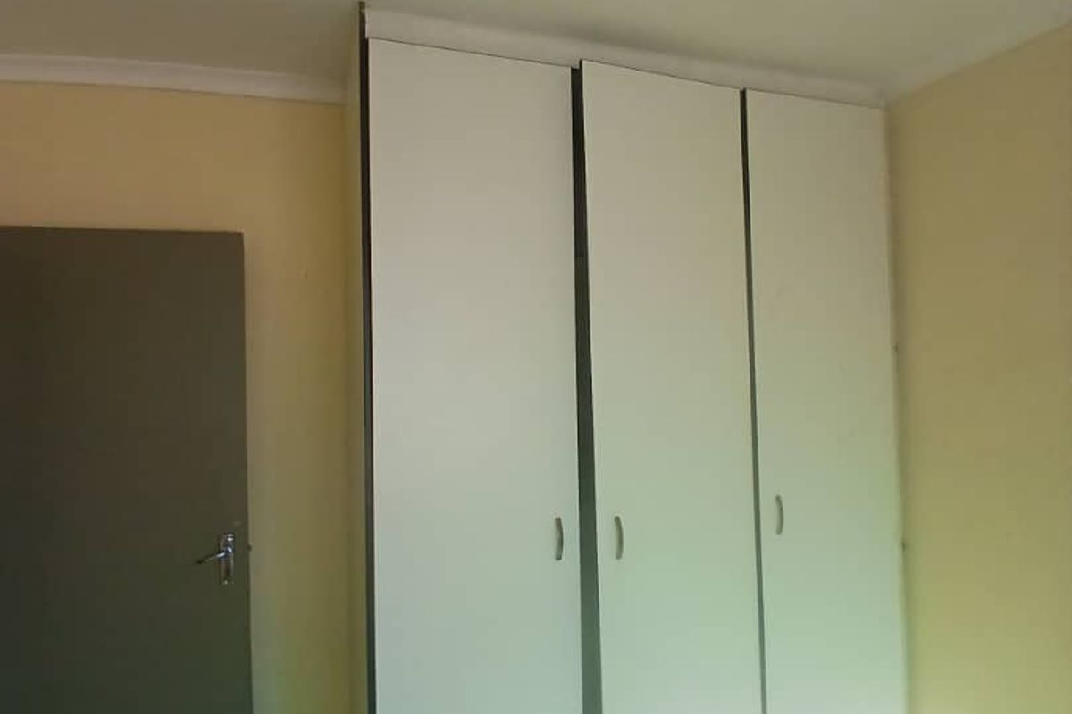 A bedroom featuring built-in white wardrobes, tiled flooring, and a standard ceiling light fixture.