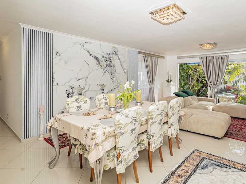 Spacious open-plan living and dining area featuring polished tile flooring, a striking marble-look feature wall, and elegant crystal ceiling lighting.