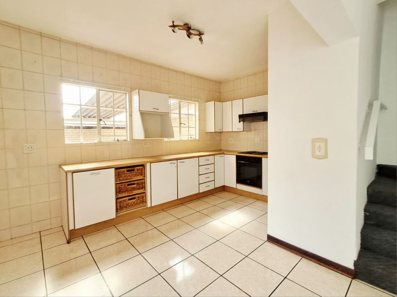 A functional kitchen featuring white built-in cabinetry, tiled backsplash, laminate countertops, and integrated cooking appliances, offering a clean and practical workspace.