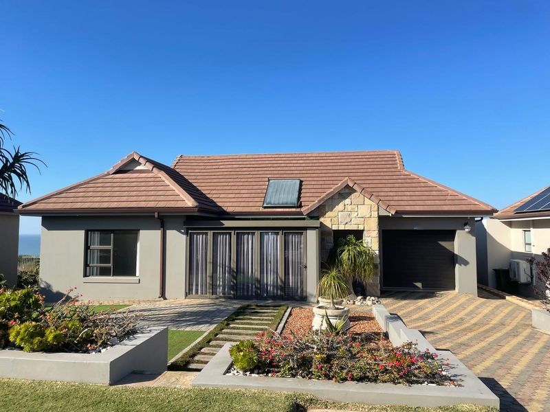 A well-maintained single-story home featuring a tiled roof, stone facade accents, a paved driveway, and a modern garage door.