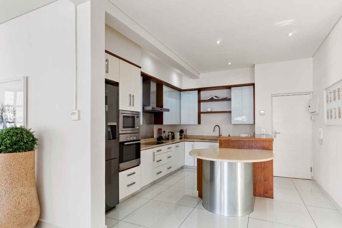 Modern kitchen featuring sleek cabinetry, integrated stainless steel appliances, a built-in oven, extractor fan, and a central breakfast island with a stone countertop.