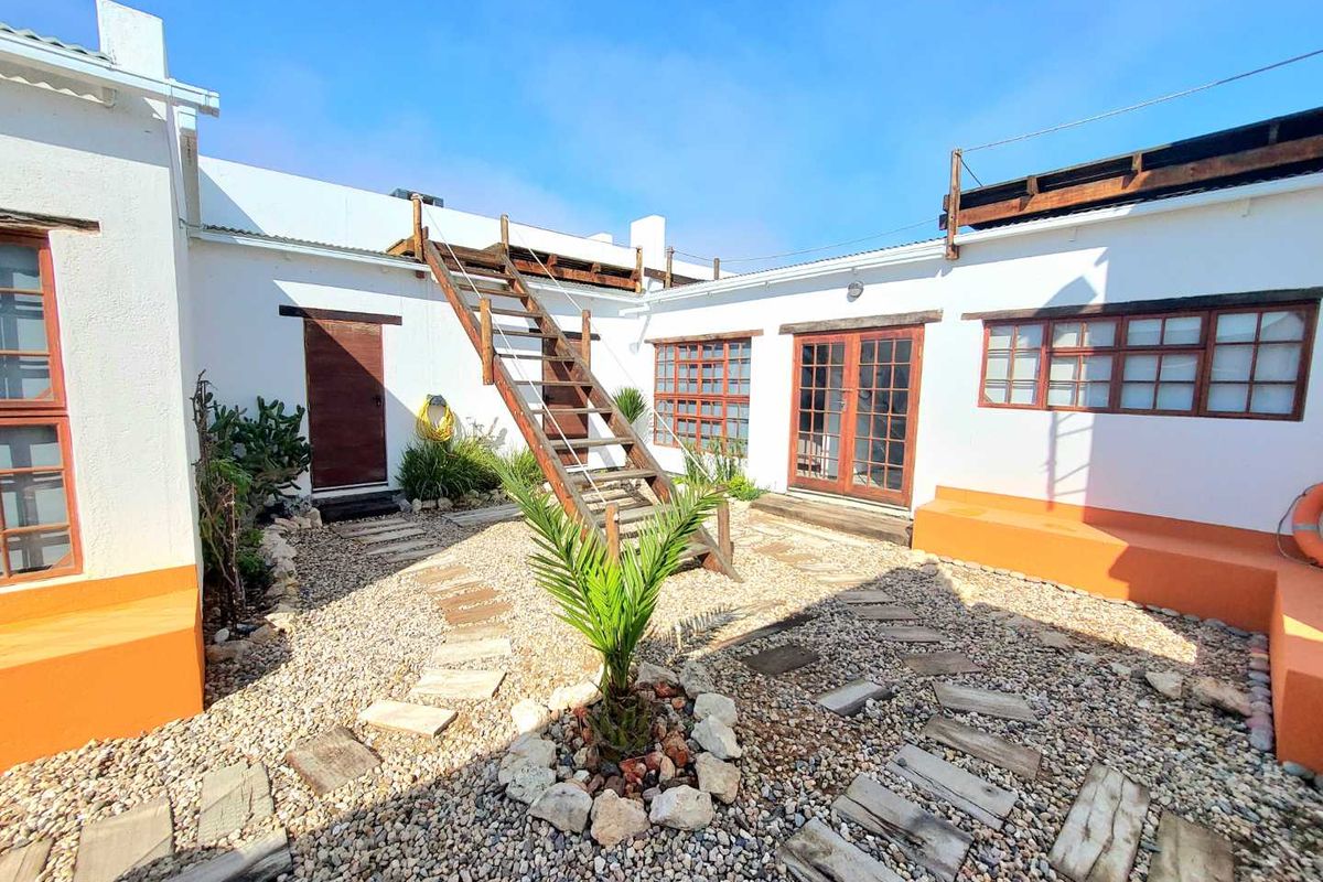 A rear courtyard featuring a gravel surface, stone stepping paths, built-in bench seating, and a wooden staircase leading to an upper level.