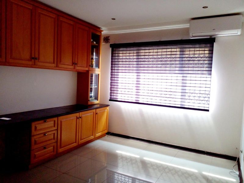 A bright, empty living space featuring extensive built-in wooden cabinetry with granite countertops, tiled flooring, and a wall-mounted air conditioning unit.