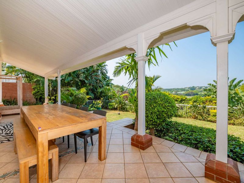 A spacious covered patio featuring tiled flooring, timber support posts with decorative brackets, and a tongue and groove ceiling, overlooking a lush garden.