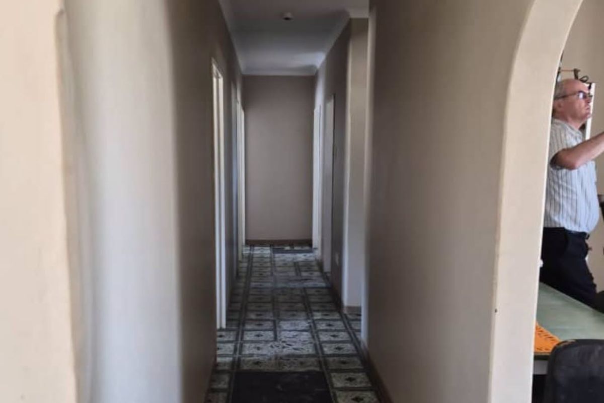 A long residential hallway featuring an arched entrance and patterned floor tiles, leading to multiple rooms.