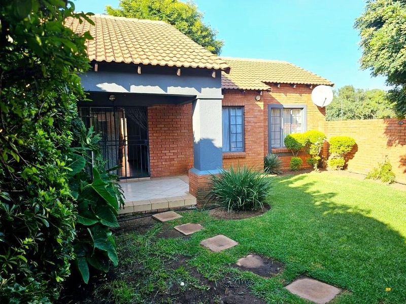 Rear view of the townhouse featuring a covered patio, brick exterior, tiled roof, and a private garden with a boundary wall.