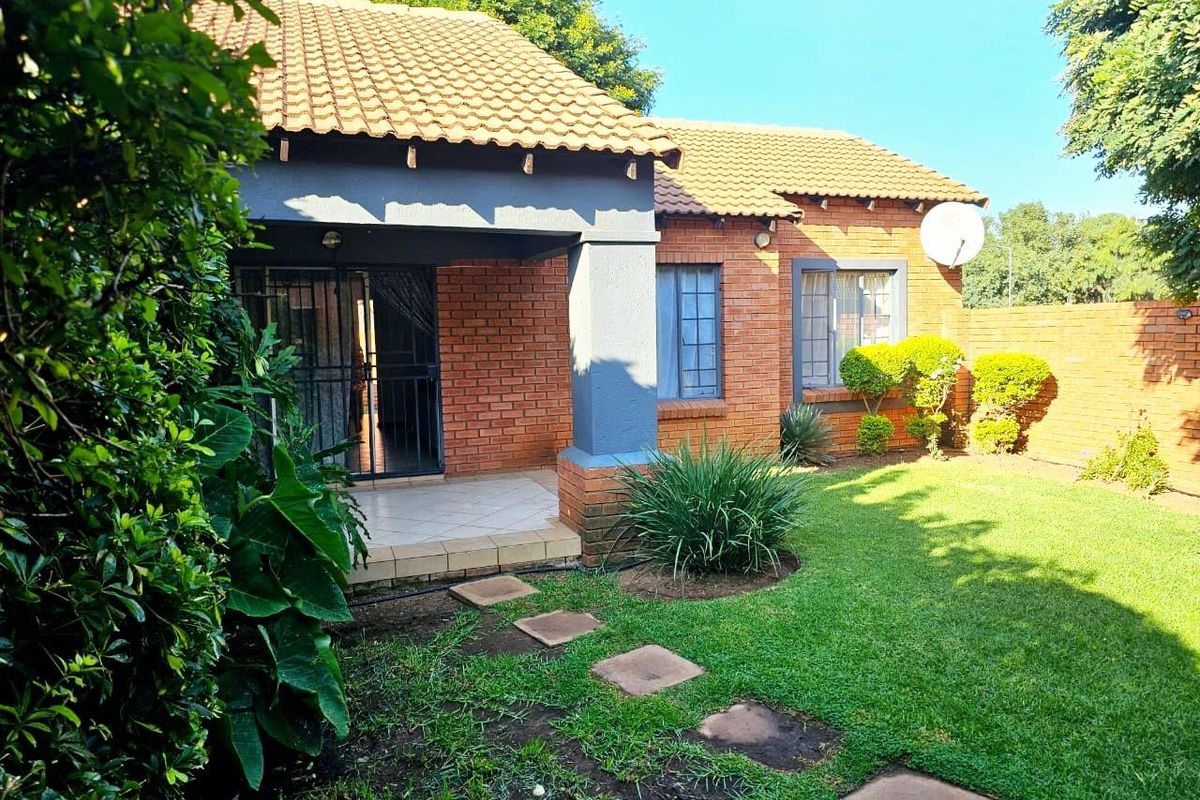Rear view of the townhouse featuring a covered patio, brick exterior, tiled roof, and a private garden with a boundary wall.