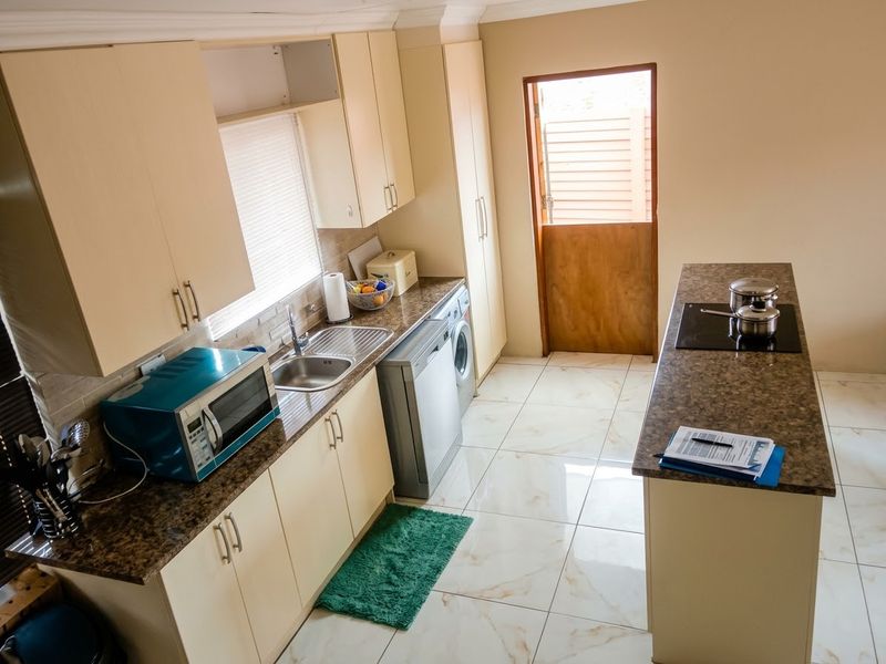 A functional kitchen featuring laminate cabinetry, granite countertops, a built-in hob, and tiled flooring, with direct access to an outdoor area via a stable door.
