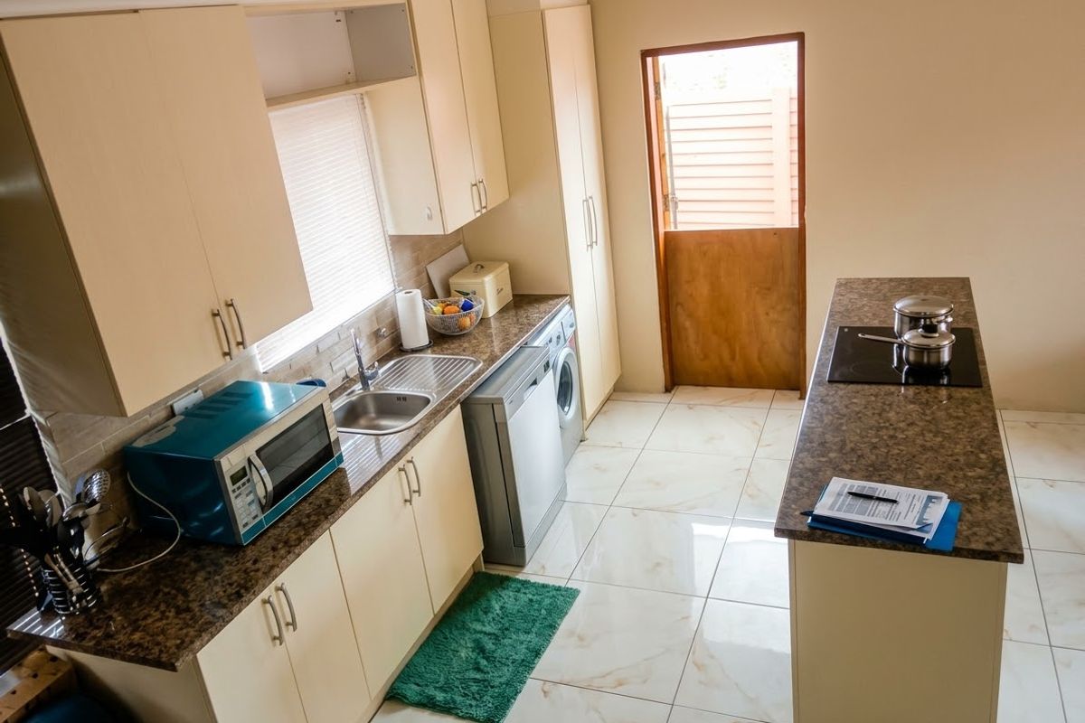 A functional kitchen featuring laminate cabinetry, granite countertops, a built-in hob, and tiled flooring, with direct access to an outdoor area via a stable door.