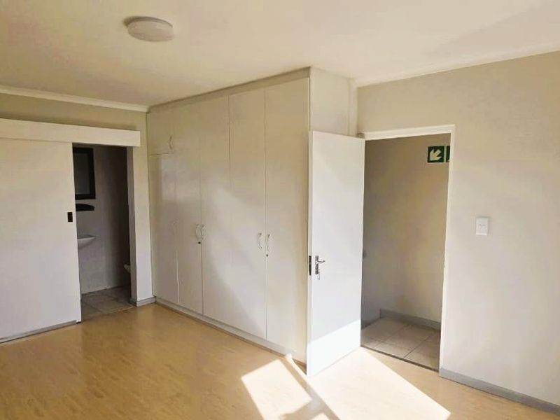 An empty bedroom featuring light-toned laminate flooring, built-in cupboards, and access to an en-suite bathroom.