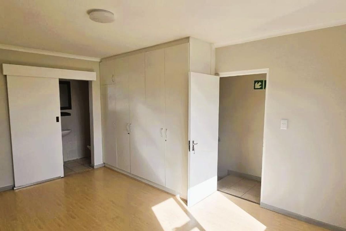 An empty bedroom featuring light-toned laminate flooring, built-in cupboards, and access to an en-suite bathroom.
