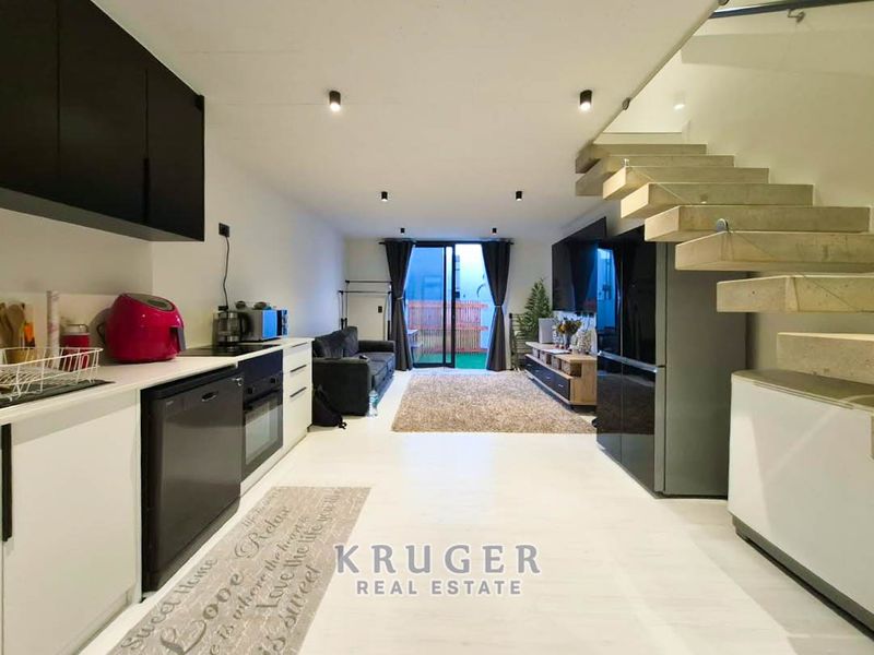Modern open-plan living area featuring a sleek kitchen, floating staircase with glass balustrade, and sliding doors leading to an outdoor space.